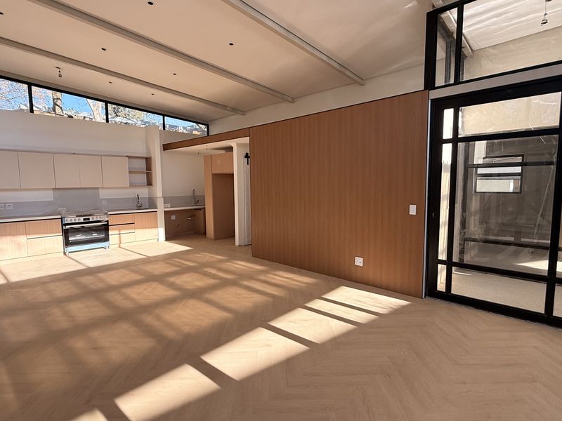 Spacious open-plan living and kitchen area featuring modern light wood cabinetry, herringbone flooring, and high ceilings with clerestory windows for abundant natural light.