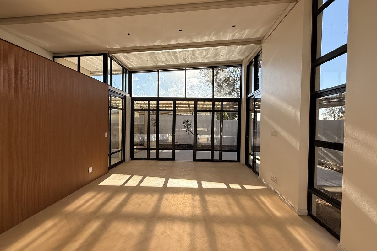 A bright, modern living area featuring floor-to-ceiling windows, elegant herringbone timber flooring, and warm wood wall paneling, offering a spacious and contemporary feel.