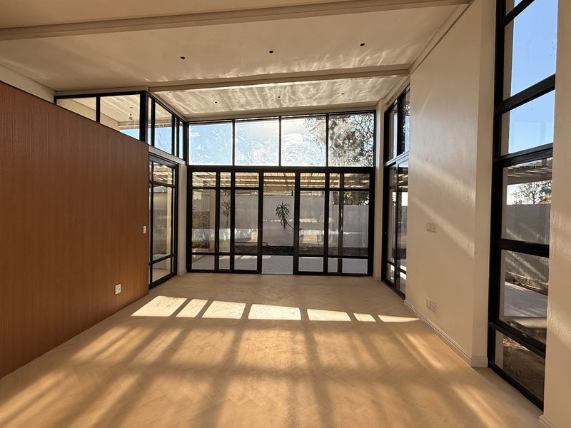 A bright, modern living area featuring floor-to-ceiling windows, elegant herringbone timber flooring, and warm wood wall paneling, offering a spacious and contemporary feel.