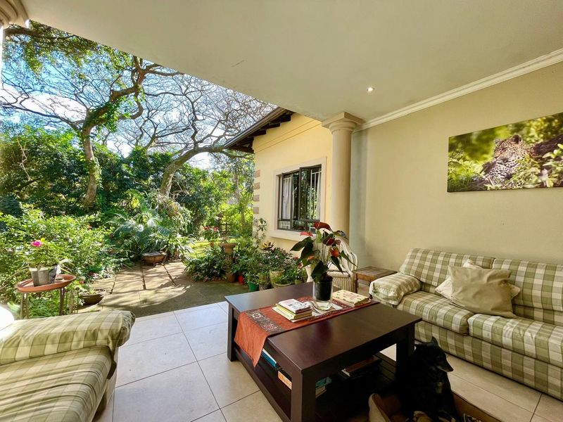 A covered patio area featuring tiled flooring, a decorative column, and direct access to a lush, landscaped garden.