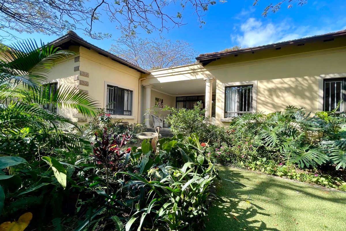 Rear view of the house featuring a covered patio area, established garden, and classic architectural details including stone quoins and columns.