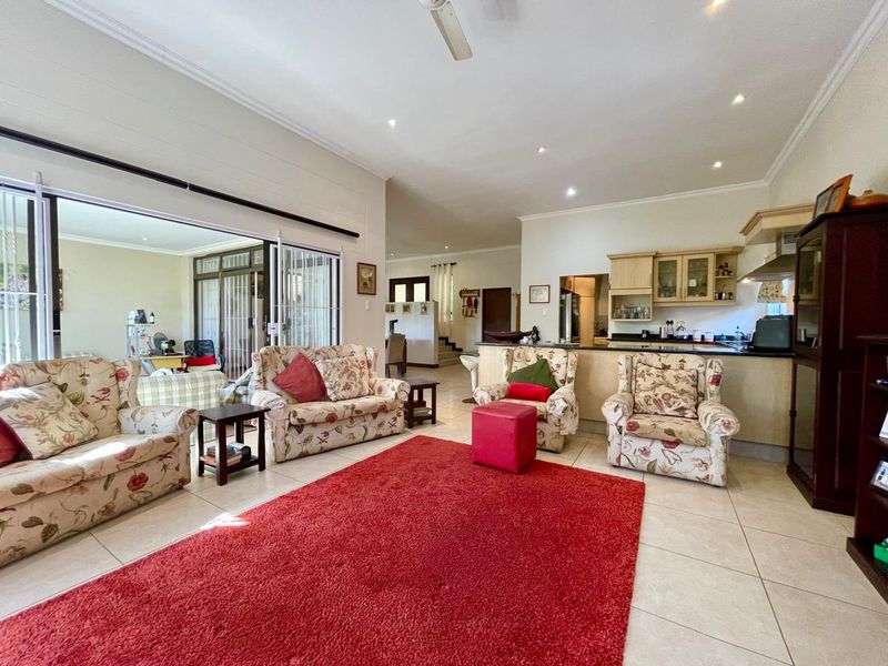 Spacious open-plan living area featuring tiled floors, recessed lighting, and a functional kitchen with granite countertops, seamlessly connecting to an outdoor patio space.