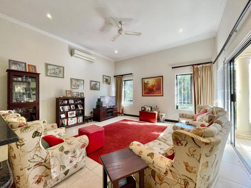 A spacious living room featuring tiled flooring, a ceiling fan, split system air conditioning, and large sliding glass doors providing natural light.