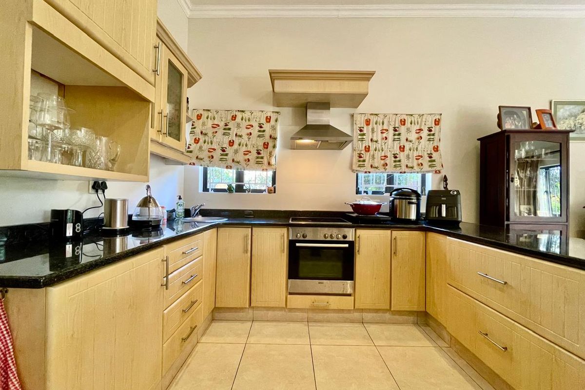 A functional kitchen featuring light wood cabinetry, granite countertops, built-in oven, extractor fan, and ceramic tile flooring.