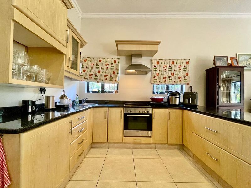 A functional kitchen featuring light wood cabinetry, granite countertops, built-in oven, extractor fan, and ceramic tile flooring.