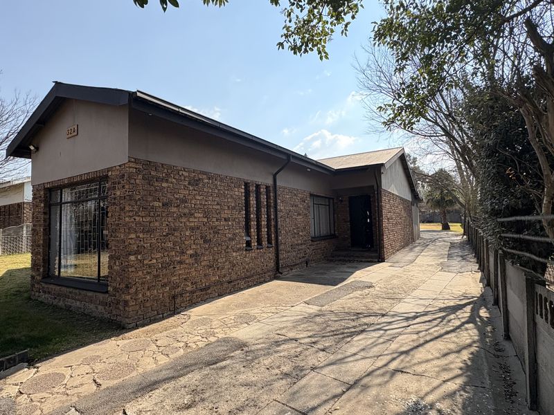 Front exterior view of a face-brick house featuring a concrete driveway, secure window bars, and a surrounding precast boundary wall.