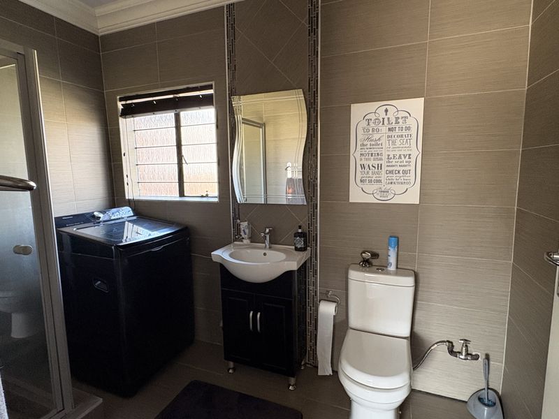 A modern bathroom featuring tiled walls, a vanity cabinet with a basin, a toilet, and a glass-enclosed shower area.