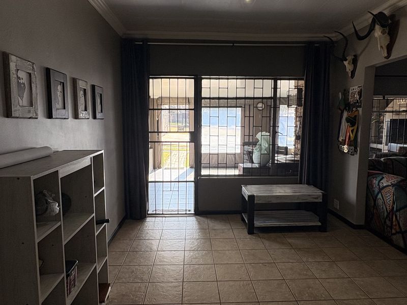 A living area featuring tiled flooring, a glossy ceiling with recessed lighting, and direct access to an enclosed patio through a security gate.
