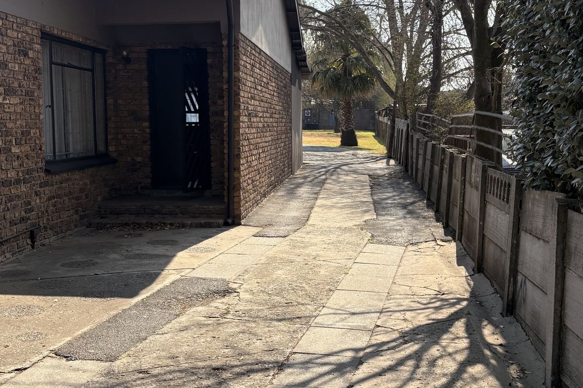 A side exterior view of the property featuring a face brick facade, concrete paving, and a precast boundary wall.