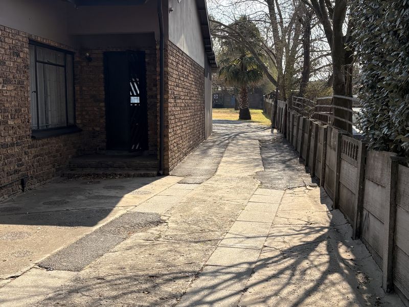 A side exterior view of the property featuring a face brick facade, concrete paving, and a precast boundary wall.