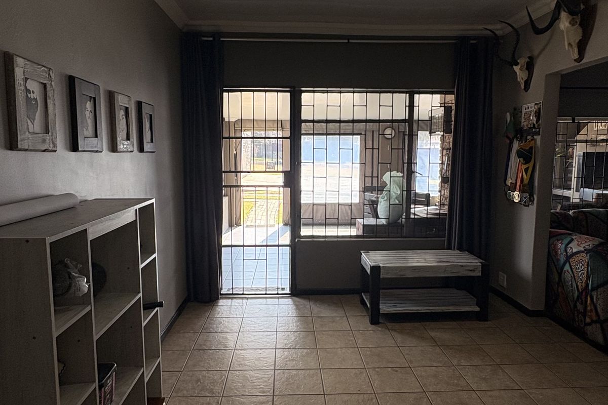 A living area featuring tiled flooring, a glossy ceiling with recessed lighting, and direct access to an enclosed patio through a security gate.