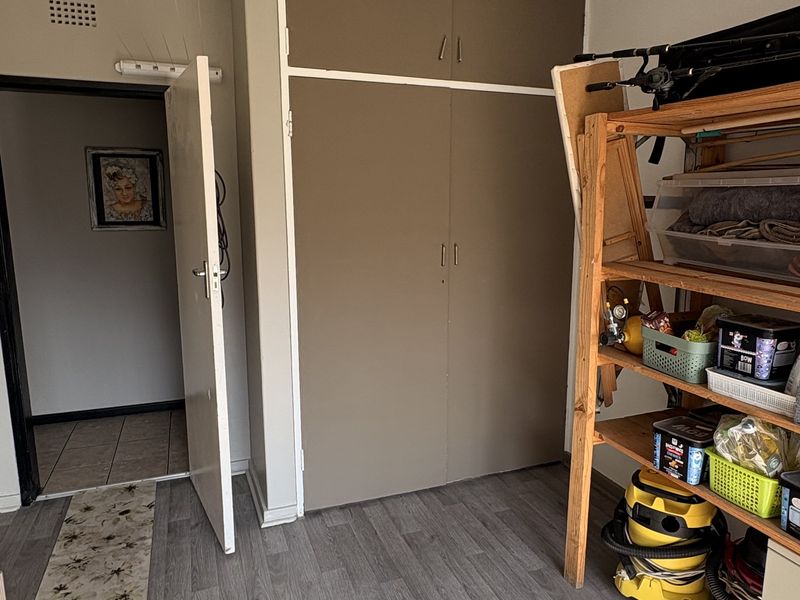 A bedroom featuring laminate flooring and a built-in cupboard with overhead storage, providing functional storage space.