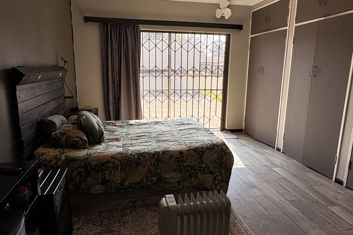 Spacious bedroom featuring built-in cupboards, laminate flooring, a ceiling fan, and a sliding glass door with security gate leading to the exterior.