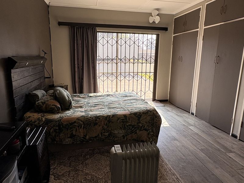 Spacious bedroom featuring built-in cupboards, laminate flooring, a ceiling fan, and a sliding glass door with security gate leading to the exterior.