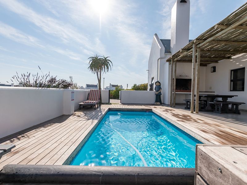 Outdoor pool area featuring timber decking, a covered patio with a built-in braai, and a masonry boundary wall.