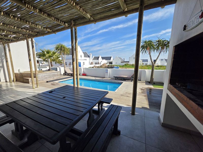Outdoor entertainment area featuring a swimming pool, timber decking, covered patio with a built-in braai, and views of the surrounding estate.