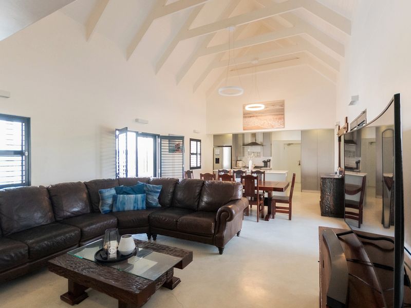Spacious open-plan living and dining area featuring high vaulted ceilings with exposed rafters, polished concrete floors, and a modern integrated kitchen.