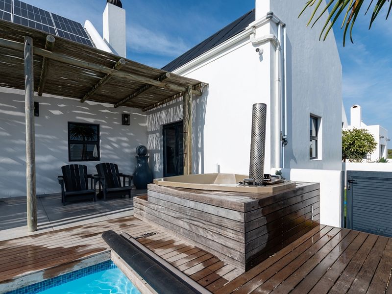 Outdoor patio area featuring a wooden pergola, built-in hot tub, and wooden decking adjacent to a swimming pool.