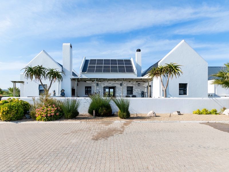 A well-maintained single-story house featuring a white facade, solar panels, a covered pergola entrance, and a paved driveway.