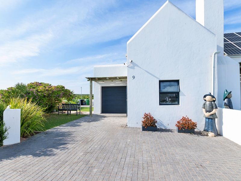 Front elevation of a white-walled house featuring a paved driveway, garage access, and roof-mounted solar panels.