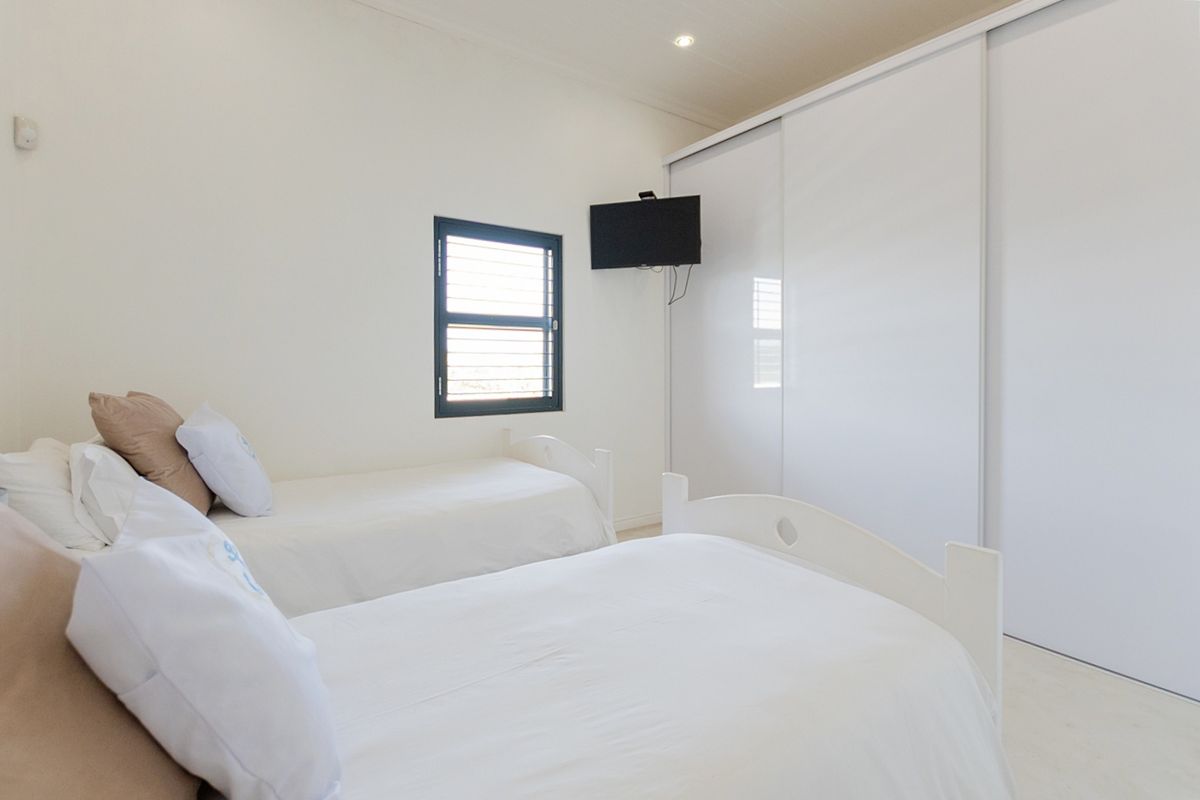 A bright bedroom featuring a large built-in sliding door wardrobe, louvered window, and recessed ceiling lighting.