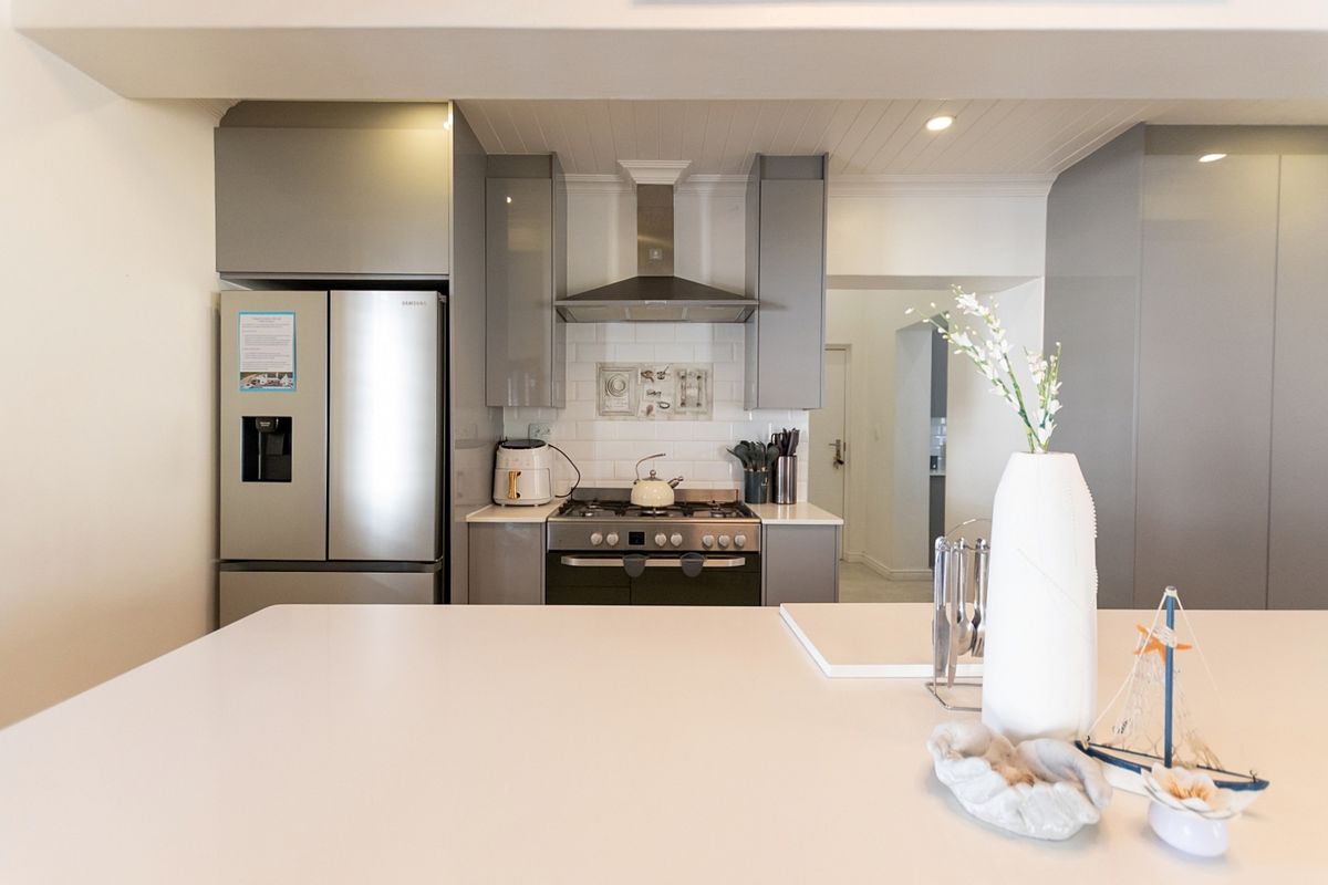 Modern kitchen featuring sleek grey cabinetry, a gas stove with extractor fan, subway tile backsplash, and a spacious stone island countertop.