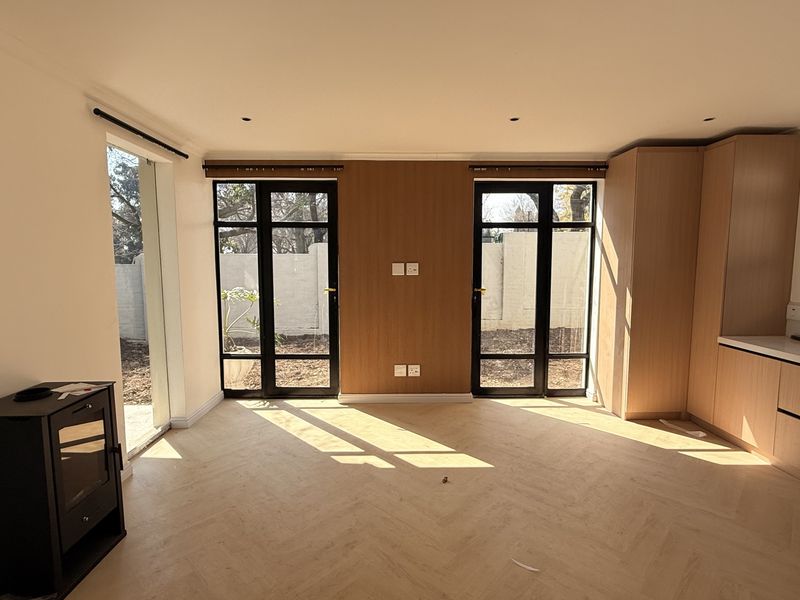 Bright open-plan living and kitchen area featuring herringbone timber flooring, modern black-framed glass doors, and a sleek built-in fireplace.