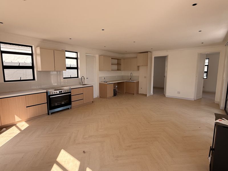 Spacious open-plan living and kitchen area featuring modern light wood cabinetry, herringbone timber flooring, and a built-in fireplace, offering a bright and versatile layout.