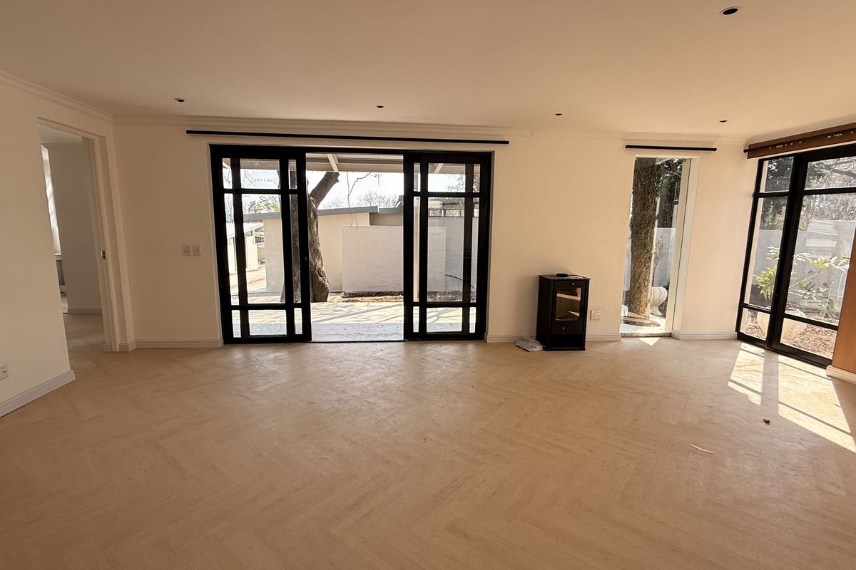 Spacious living area featuring elegant herringbone timber flooring, modern black-framed sliding doors, and recessed lighting, offering a bright and contemporary open-plan feel.
