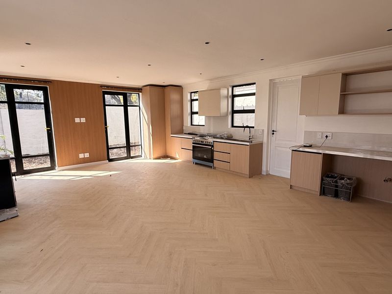 Spacious open-plan living and kitchen area featuring modern herringbone timber flooring, sleek cabinetry, and large glass doors leading to the exterior.