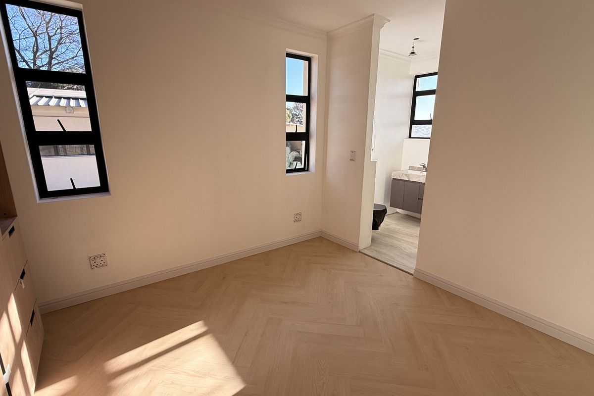 A bright, empty bedroom featuring modern herringbone timber flooring, built-in cabinetry, and direct access to an en-suite bathroom with contemporary finishes.