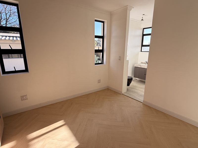 A bright, empty bedroom featuring modern herringbone timber flooring, built-in cabinetry, and direct access to an en-suite bathroom with contemporary finishes.