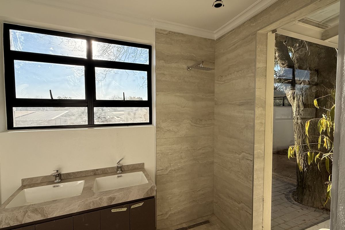 Modern bathroom featuring a double vanity with stone countertop, walk-in shower with rain shower head, and large black-framed windows.