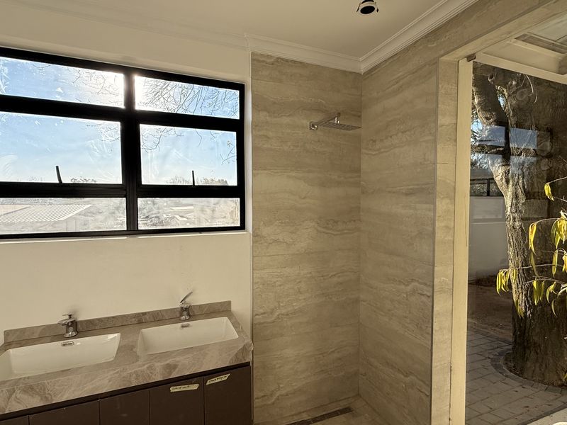 Modern bathroom featuring a double vanity with stone countertop, walk-in shower with rain shower head, and large black-framed windows.