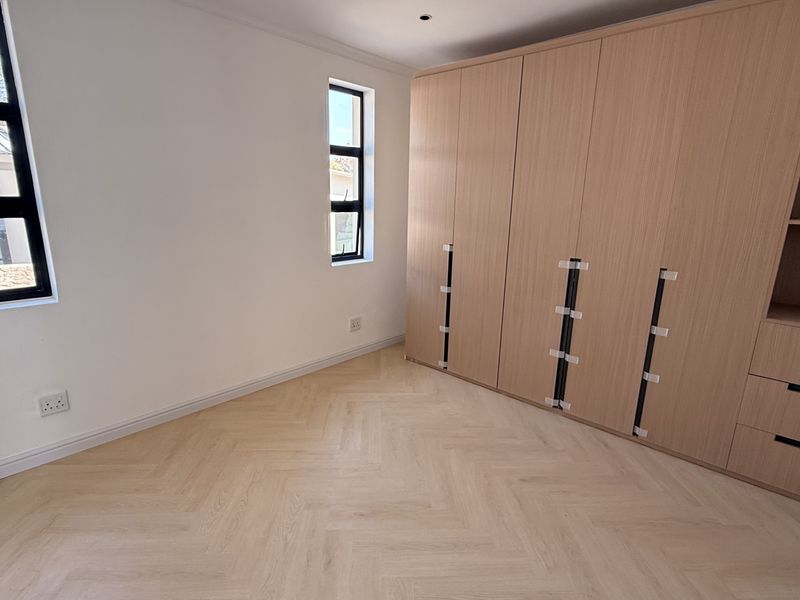 A bright, modern bedroom featuring light wood herringbone flooring and extensive built-in cabinetry with integrated shelving.
