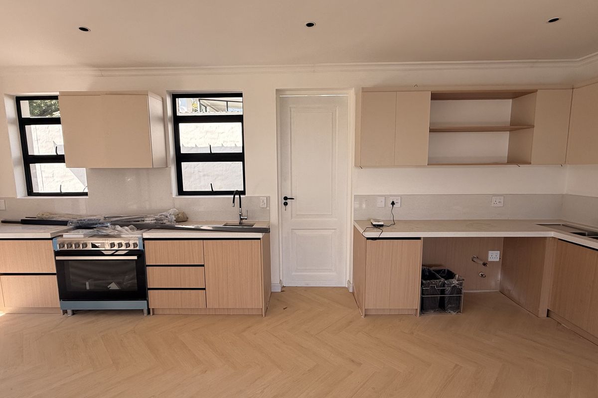 A modern, newly installed kitchen featuring light wood cabinetry, herringbone flooring, and integrated appliances, currently awaiting final finishing touches and hardware installation.