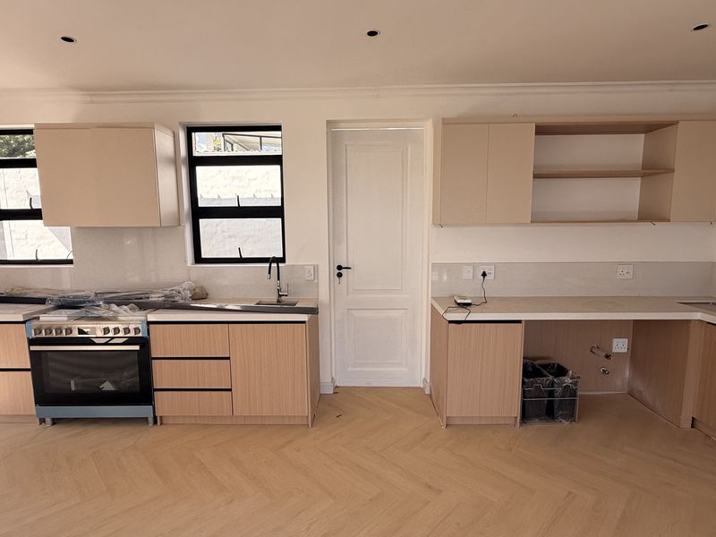 A modern, newly installed kitchen featuring light wood cabinetry, herringbone flooring, and integrated appliances, currently awaiting final finishing touches and hardware installation.