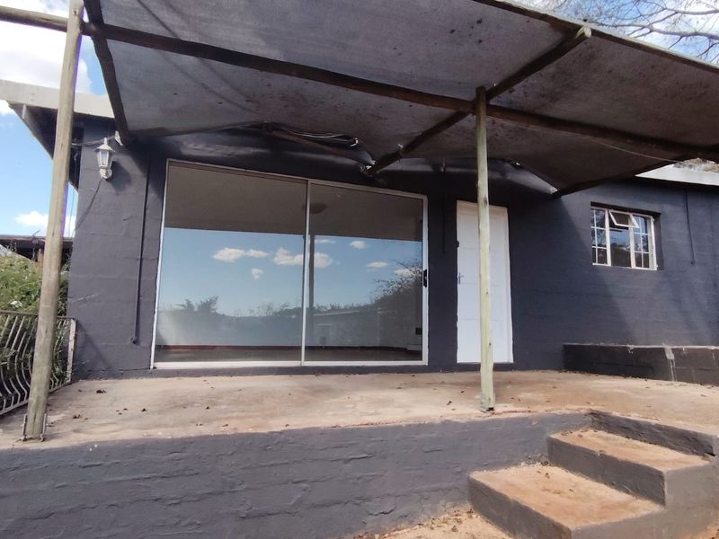 A covered patio area featuring a shade cloth canopy, concrete steps, and a sliding glass door entrance to the cottage.