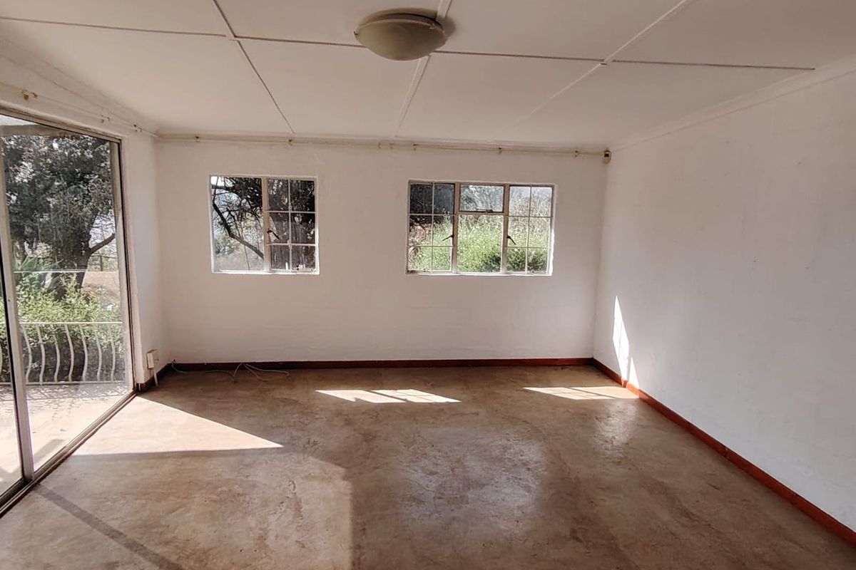 An empty, sunlit living room featuring concrete flooring, steel-framed windows, and a sliding glass door leading to an outdoor area.