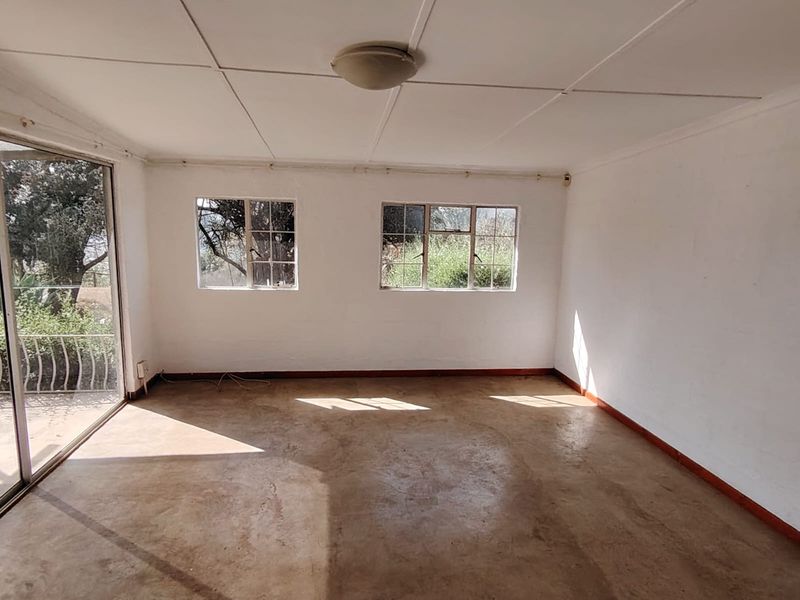 An empty, sunlit living room featuring concrete flooring, steel-framed windows, and a sliding glass door leading to an outdoor area.