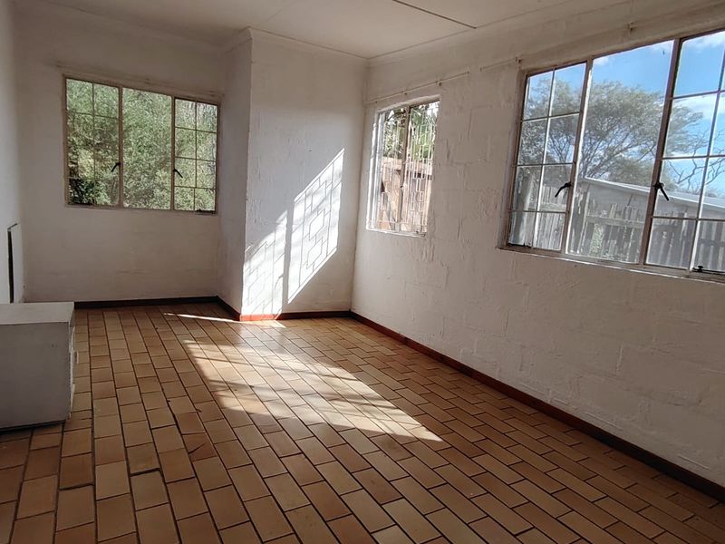 A bright, empty living area featuring terracotta tile flooring and multiple steel-framed windows, offering a blank canvas for renovation.