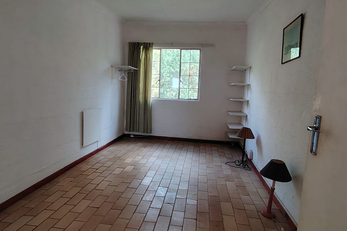 A vacant bedroom featuring terracotta tile flooring, a grid window, and wall-mounted shelving, offering a blank canvas for renovation.