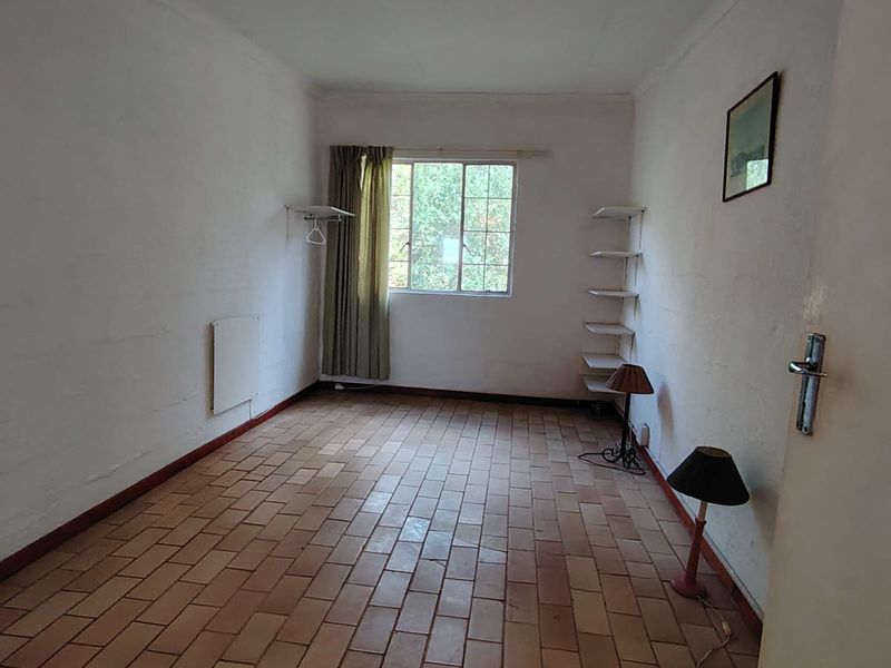 A vacant bedroom featuring terracotta tile flooring, a grid window, and wall-mounted shelving, offering a blank canvas for renovation.