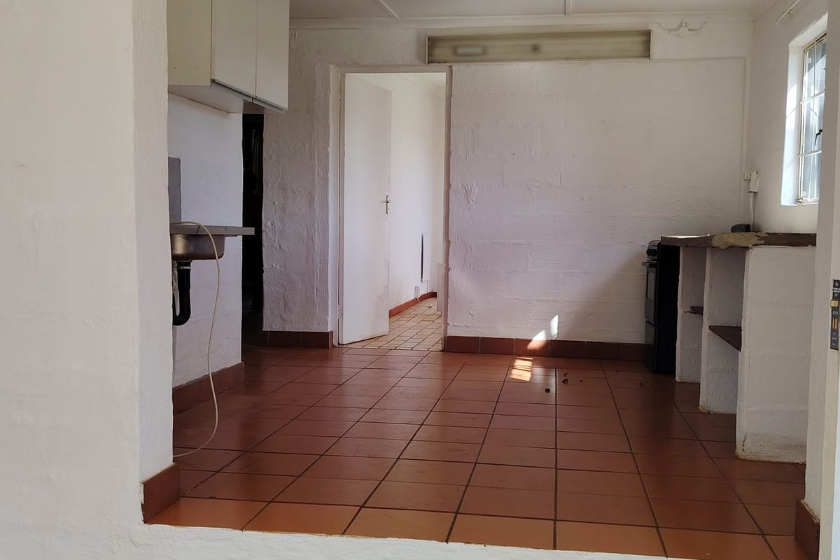 An empty, dated kitchen area featuring tiled flooring, built-in masonry shelving, and basic cabinetry, requiring renovation to modernize the space.