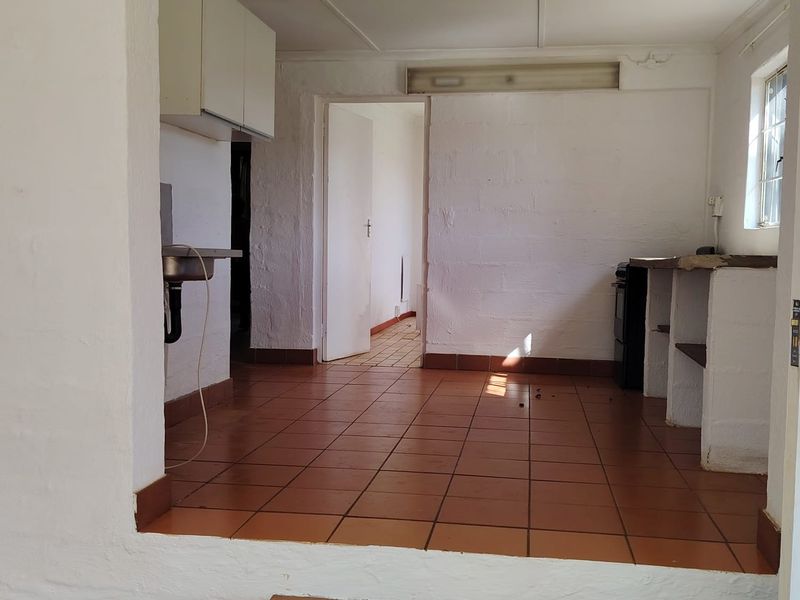 An empty, dated kitchen area featuring tiled flooring, built-in masonry shelving, and basic cabinetry, requiring renovation to modernize the space.