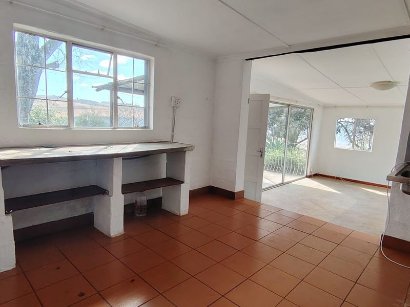 Open plan living area featuring terracotta floor tiles, built-in masonry workbench, and large windows providing natural light and access to the outdoor space.