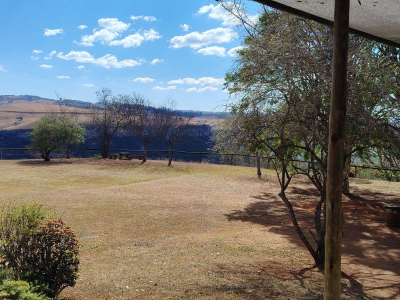 A covered outdoor patio area featuring timber support posts and shade cloth, overlooking a spacious garden with expansive rural landscape views.
