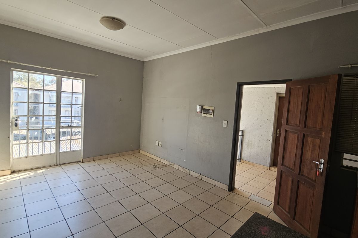 An empty living room featuring tiled flooring, a glass sliding door leading to a balcony, and a timber door leading to an adjacent space.