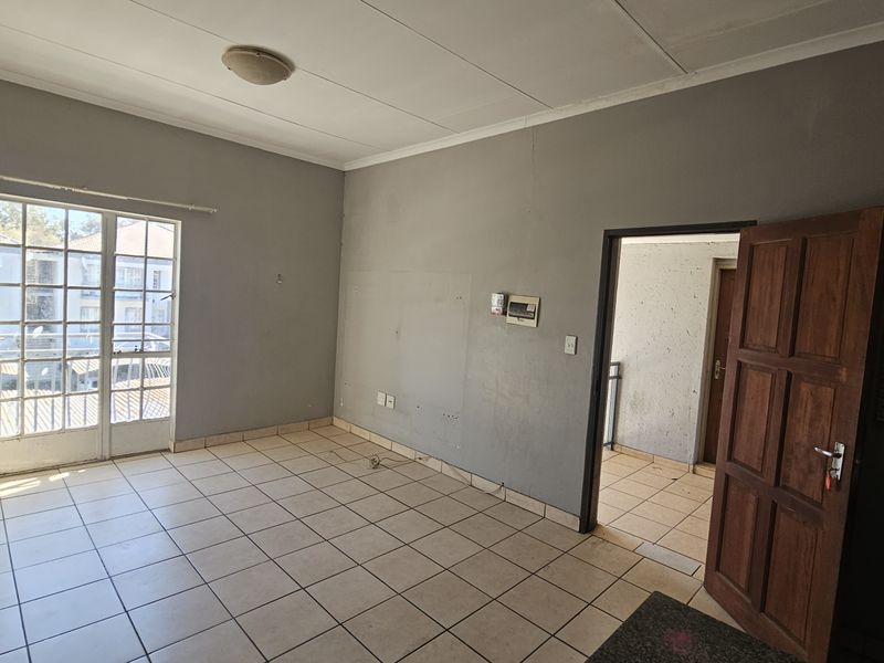 An empty living room featuring tiled flooring, a glass sliding door leading to a balcony, and a timber door leading to an adjacent space.