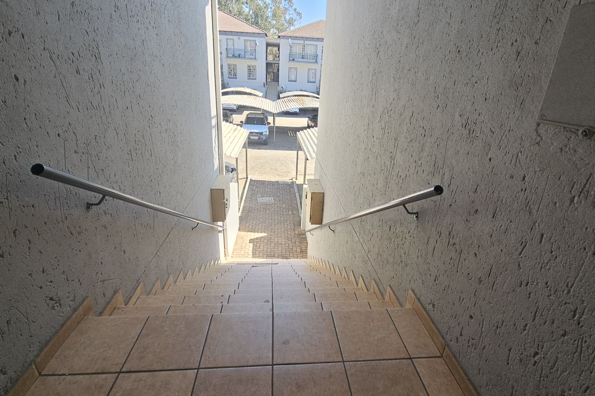 Exterior staircase with metal handrails leading down to a paved walkway and communal carport area within the apartment complex.